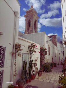 Calle del centro histórico de Polignano a Mare con casas blancas tradicionales, balcones y plantas decorando las fachadas, en la región de Puglia, Italia.