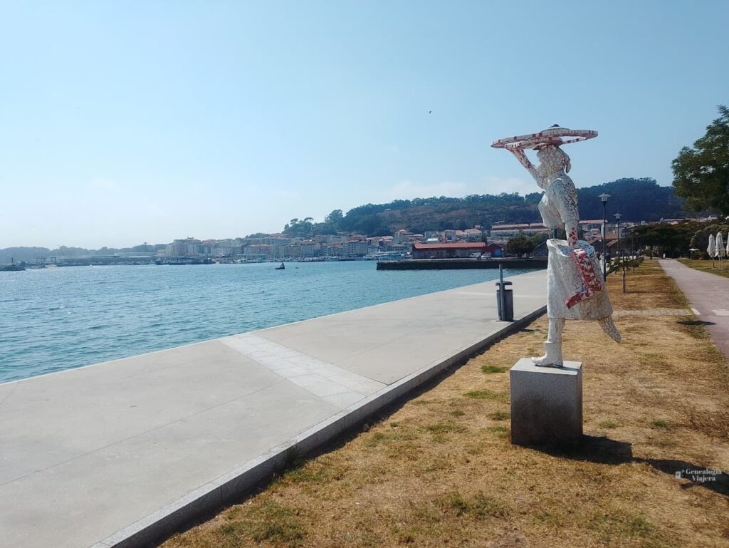 Estatua de una mariscadora junto al paseo marítimo de Cangas do Morrazo, con la ría de Vigo y el mar azul de fondo.