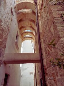 Calle estrecha del casco histórico de Polignano a Mare con pasaje de piedra y techo abovedado parcial, rodeada de casas blancas tradicionales en el centro histórico de Puglia, Italia.
