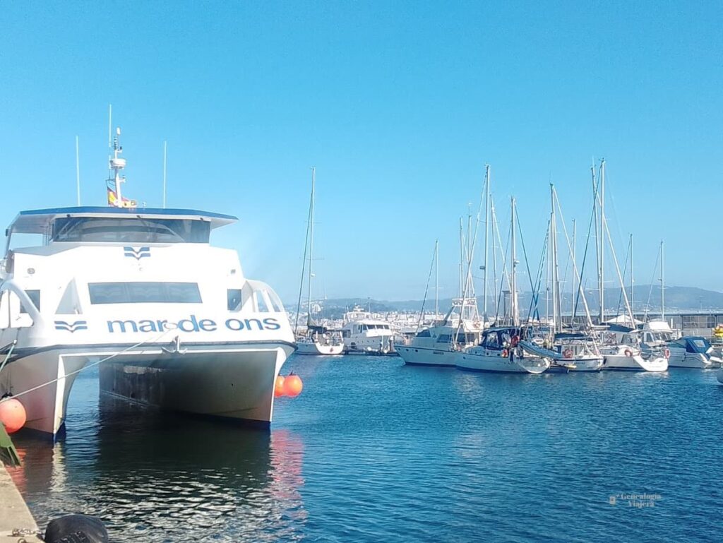 Puerto de Cangas do Morrazo con el mar azul de la ría de Vigo, barcos amarrados y un ferry de Mar de Ons junto al embarcadero.
