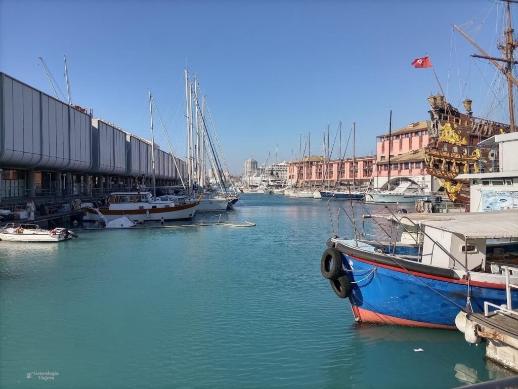 Vista del Porto Antico de Génova, con aguas turquesas, embarcaciones amarradas y edificios portuarios al fondo.