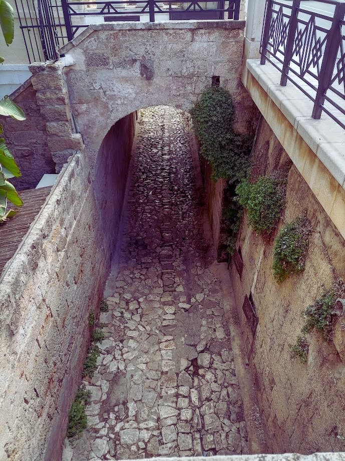 Sendero de piedra bajo el puente de Polignano a Mare que lleva hacia Cala Porto y la playa de guijarros junto al mar Adriático