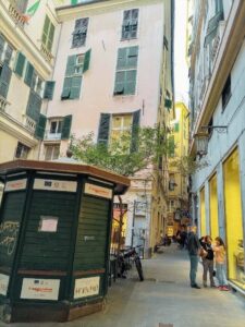 Calle del centro histórico de Génova con comercios tradicionales y vecinos conversando en la vía peatonal.