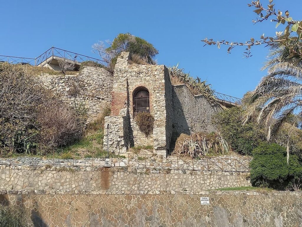 Antigua construcción entre muros de piedra en Corso Italia, con una puerta de hierro y un sendero con baranda en la parte superior