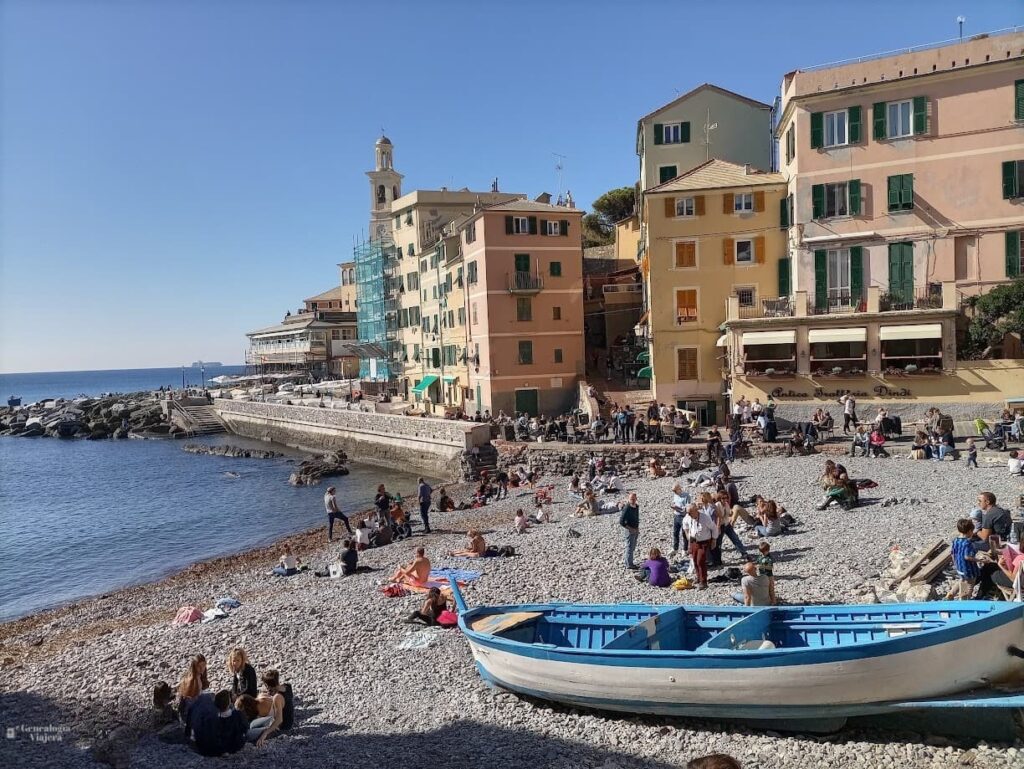 Playa del barrio de Boccadasse en Génova con un bote sobre los guijarros, personas junto al mar y las casas de colores características del antiguo pueblo de pescadores.