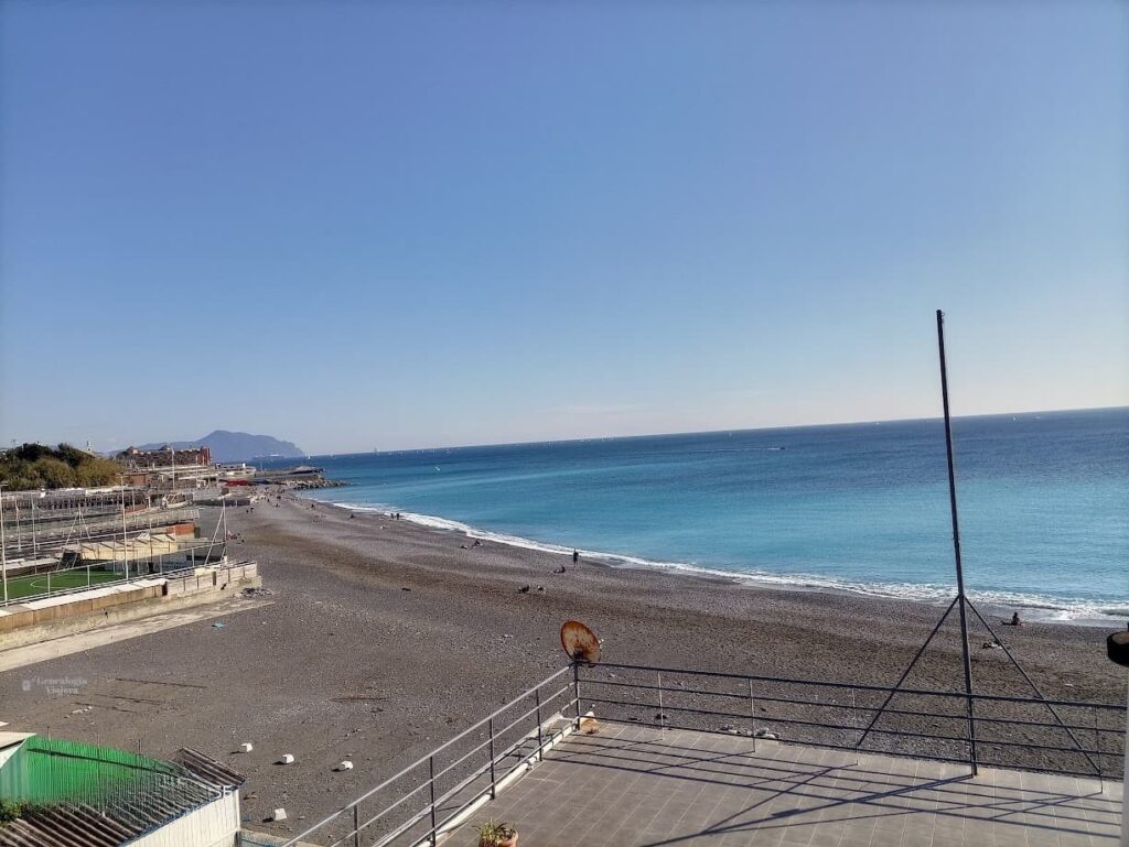 Playa del Corso Italia en Génova, con grava oscura y las aguas turquesas del mar Mediterráneo.