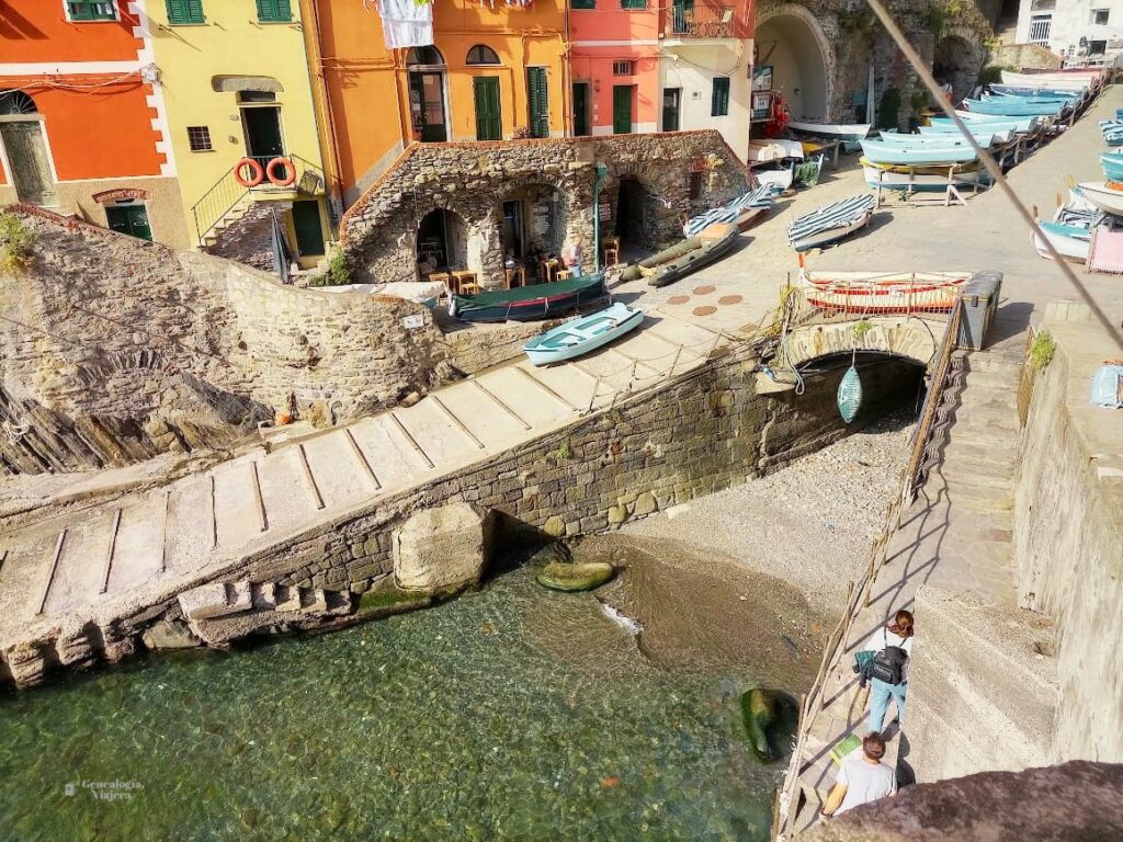 Acceso a una pequeña playa de piedras en Riomaggiore, con un túnel, un bote colgado y el mar Mediterráneo al fondo.