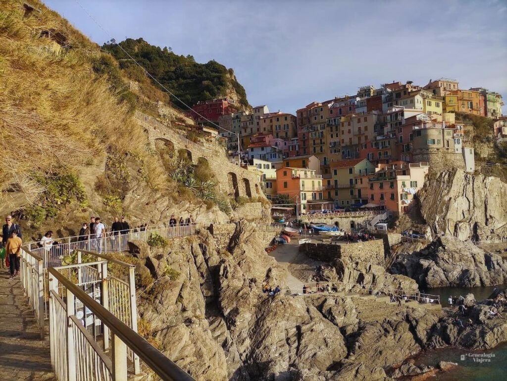  Perspectiva desde el camino de los acantilados hacia el puerto y las casas verticales de Manarola, capturando la arquitectura típica de la costa de Liguria, Italia, en un día despejado.