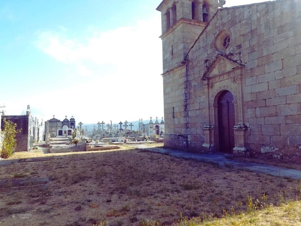 Vista lateral de la Iglesia de San Miguel de Soutopenedo y su cementerio parroquial contiguo, mostrando tumbas, cruces de piedra en el camposanto y la arquitectura exterior del templo bajo un cielo azul con nubes
