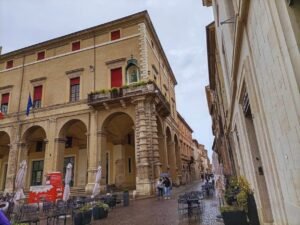 Vista del Palazzo Garampi y la Piazza Cavour en Rimini en un dia de lluvia de octubre, con gente paseando y mesas de bares den las veredas