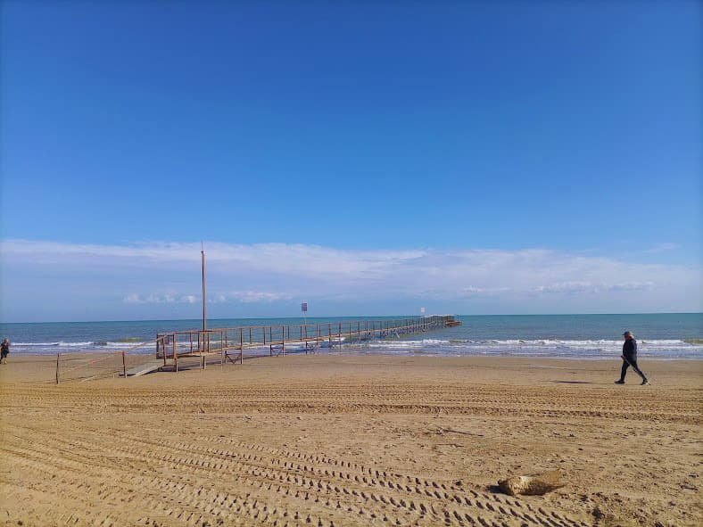 Vista de la playa de Rímini desocupada tras el fin de la temporada de verano, mostrando la arena con huellas y un muelle solitario hacia el mar.
