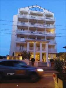 Fachada iluminada por la tarde del Le Rose Suite Hotel en Rímini, Italia, un edificio blanco y moderno con balcones frente a la calle.