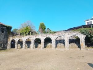 Sucesión de arcos de piedra antiguos pertenecientes a las ruinas del Monasterio de Santa María de Melón, Galicia, en un día soleado.