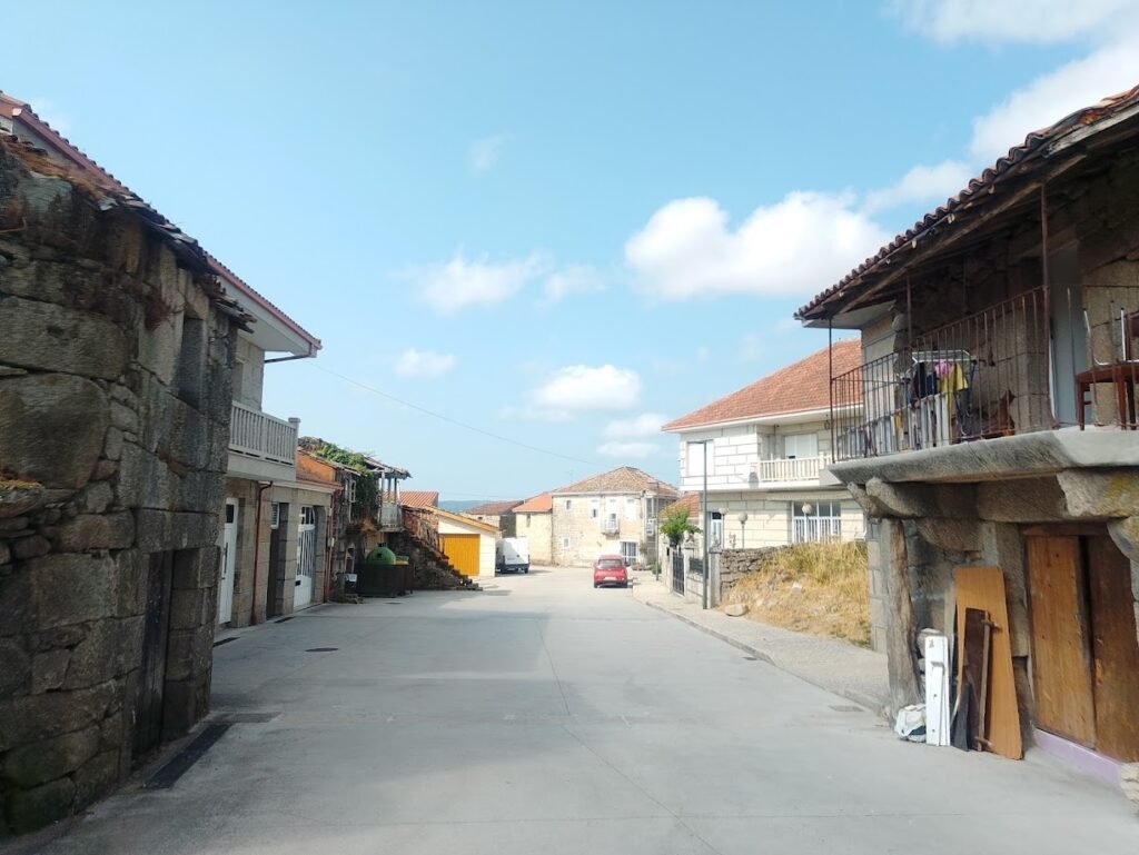 Calle tranquila en Vilar de Santos, Ourense, rodeada de casas tradicionales gallegas construidas con gruesos muros de piedra y balcones de madera.