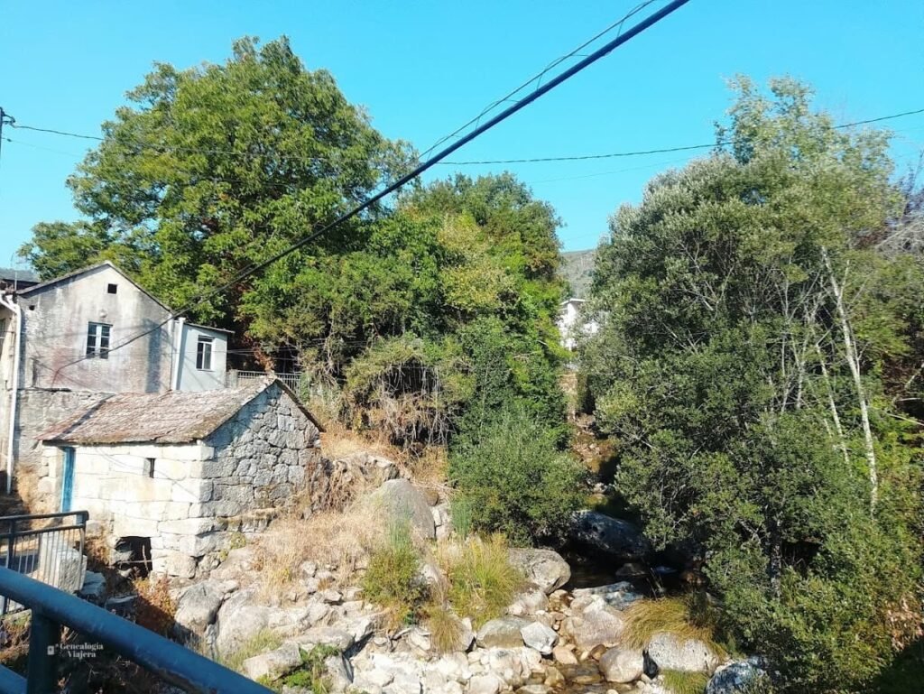 Pequeña construcción antigua de piedra junto a un arroyo con rocas rodeado de árboles verdes en el pueblo de Melón, Galicia.
