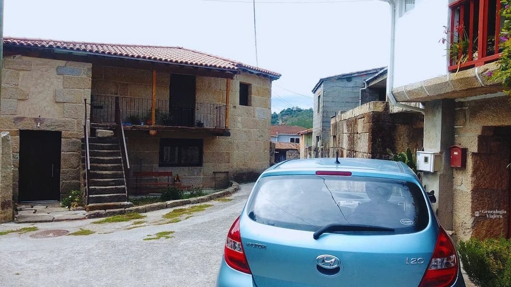 Calle asfaltada a en la aldea de Paradela rodeada de casas tradicionales y un auto azul