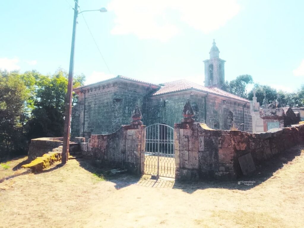 Vista exterior de la Iglesia de Santa Baia de Banga en O Carballiño, mostrando sus muros de sillería de piedra, el recinto amurallado y el acceso de reja metálica.