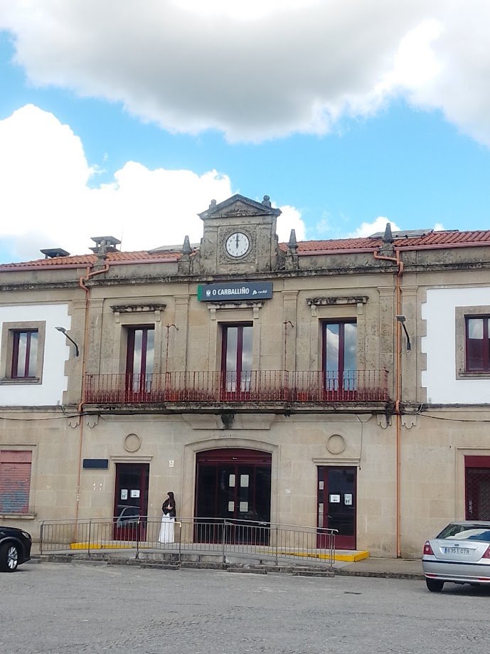 Fachada de piedra de la estación de tren de O Carballiño con su reloj clásico en la parte superior y el cartel oficial de Adif.