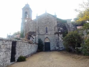 • 
	• Fachada principal de piedra rústica de la iglesia del Monasterio de Santa María de Melón en Ourense, con una gran puerta oscura, una ventana ojival central y la torre del campanario a la izquierda.
