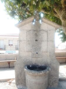 Monumental fuente de piedra grabada con el año 1951 situada en una plaza arbolada de Vilar de Santos, Ourense.