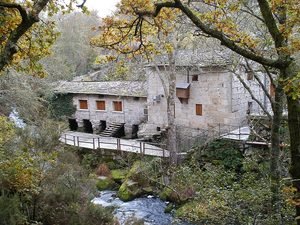 Antiguo molino de piedra restaurado junto al río Arenteiro, rodeado de árboles en otoño.
