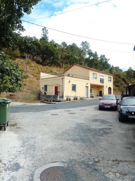 Ruta de entrada a la aldea de Paradela en Ourense con una casa amarilla al fondo y autos estacionados.